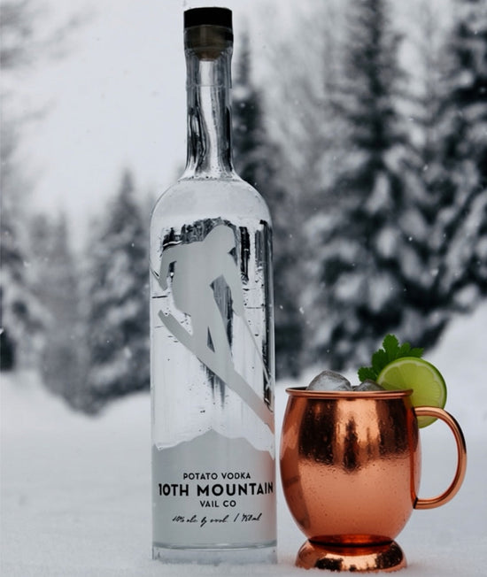 Bottle of 10th Mountain Vodka with a copper mug in a snowy setting